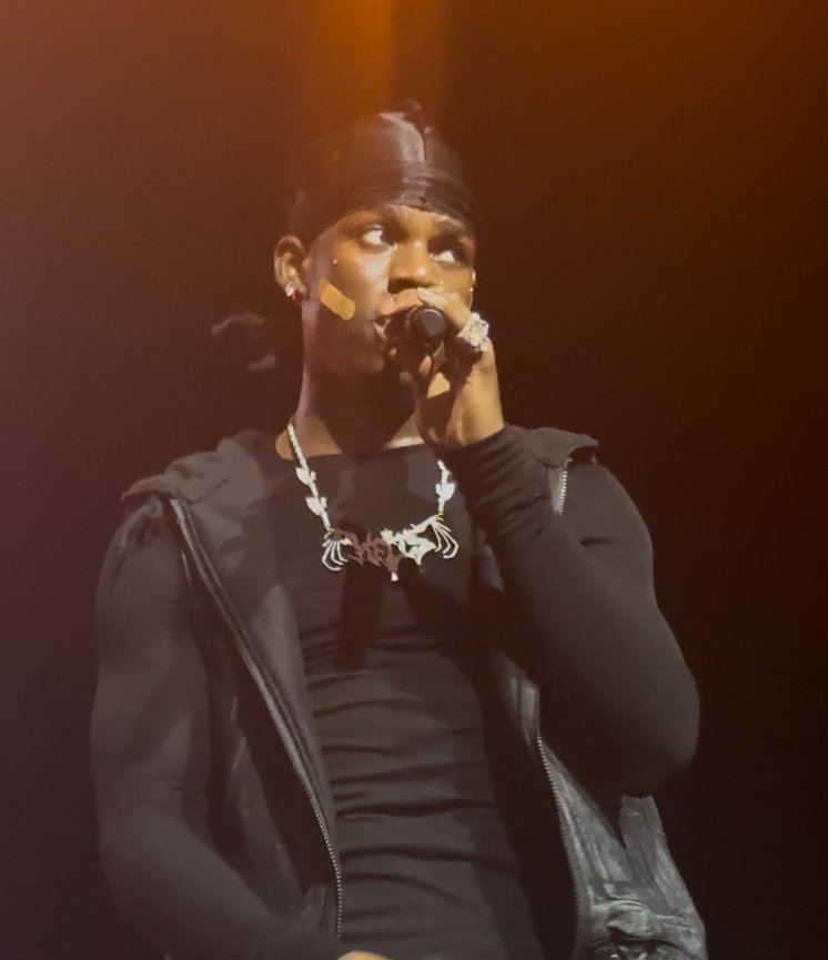 Rema singing into a microphone on stage in Boston