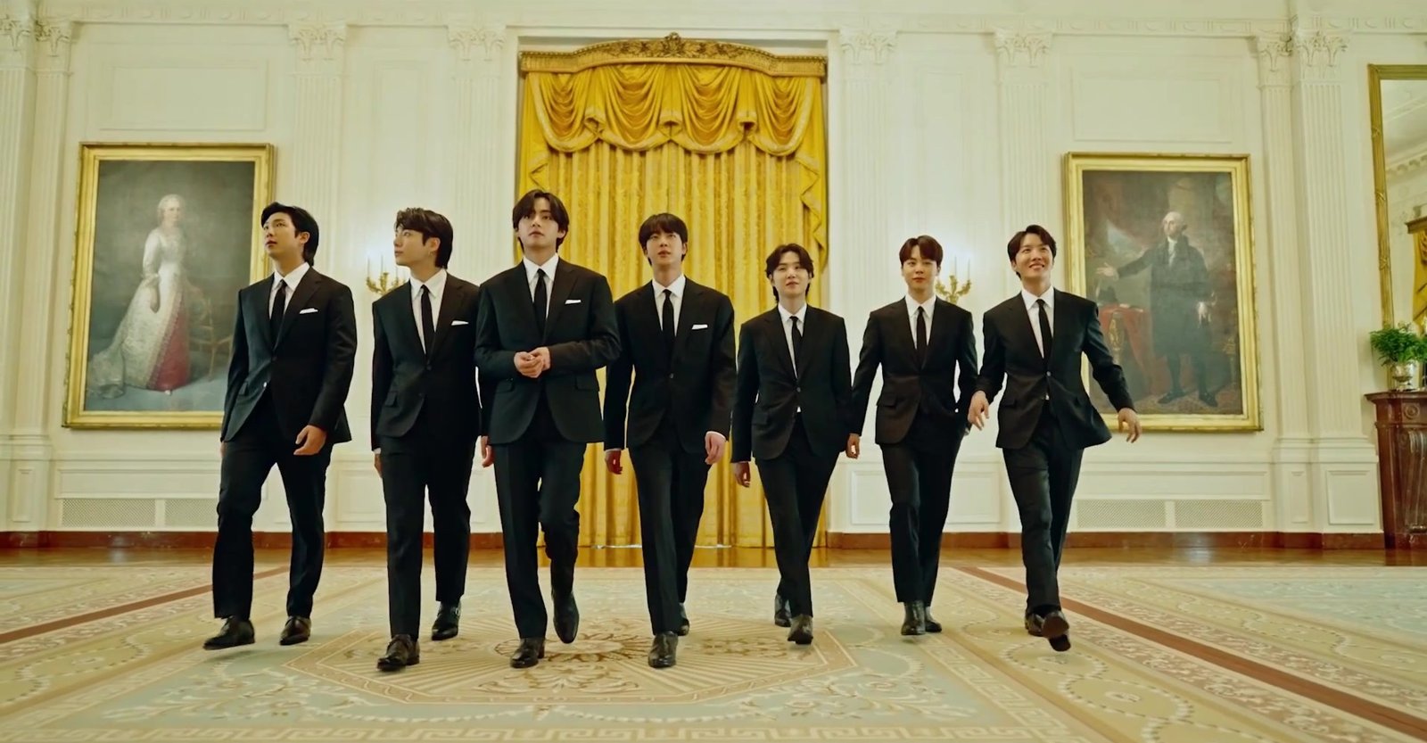 The seven members of BTS walking through the White House in dark suits
