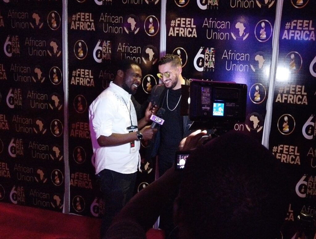 A presenter interviews guests in front of an AFRIMA and African Union backdrop