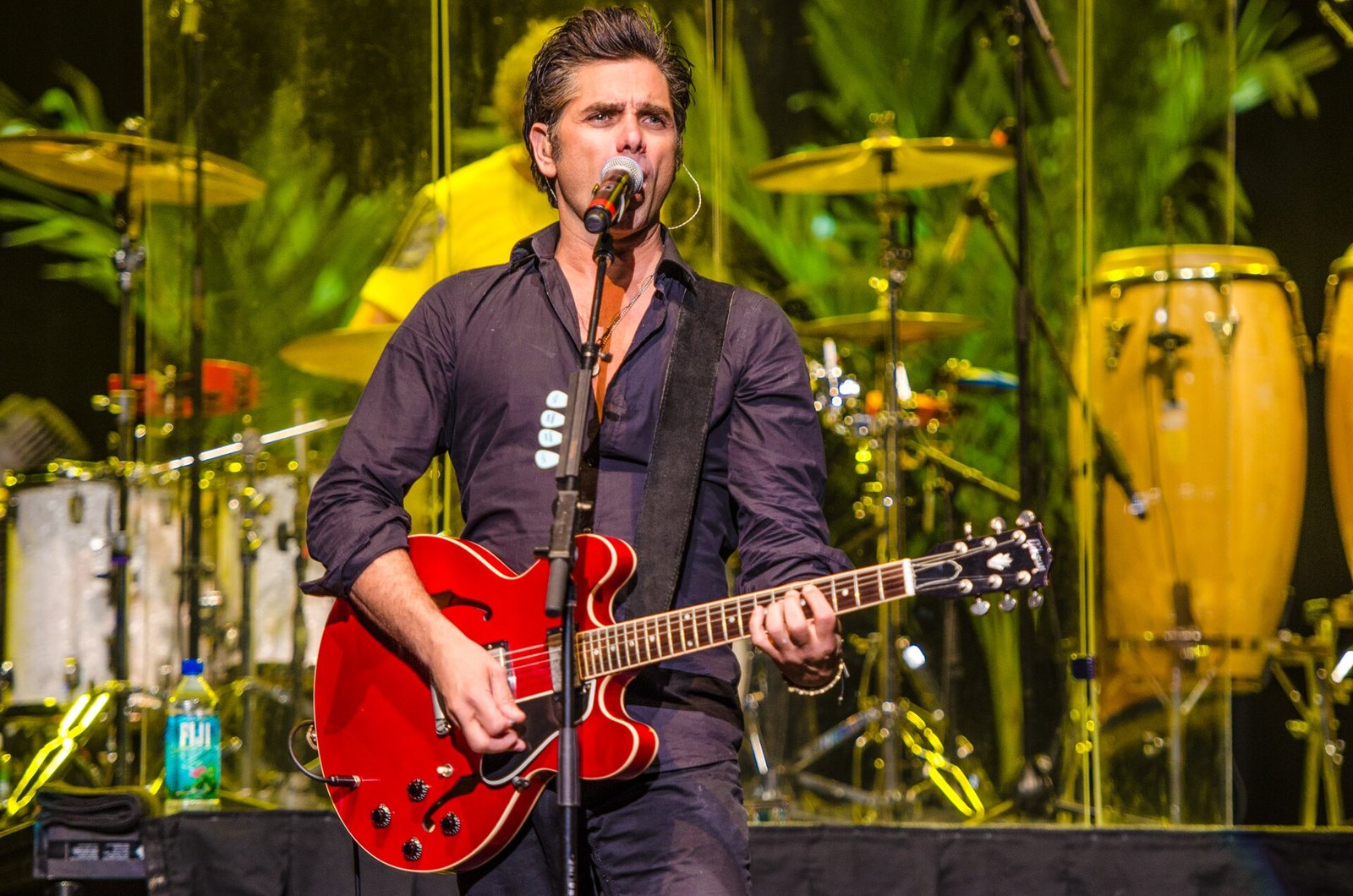 John Stamos playing a red guitar on stage with the Beach Boys